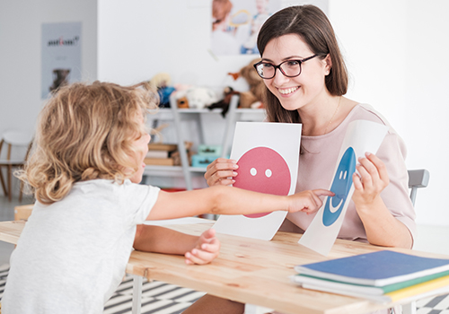 Smiling counselor holding pictures during meeting with young patient with autism